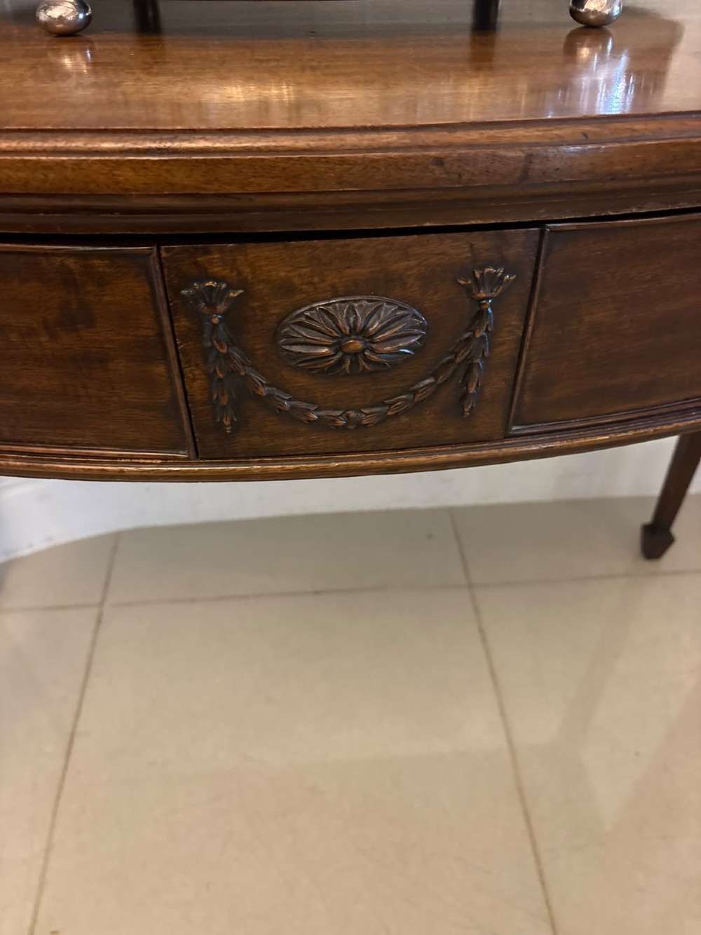 An Edwardian mahogany console table featuring a serpentine front, carved central motif, brass handles, and square tapered legs. View V