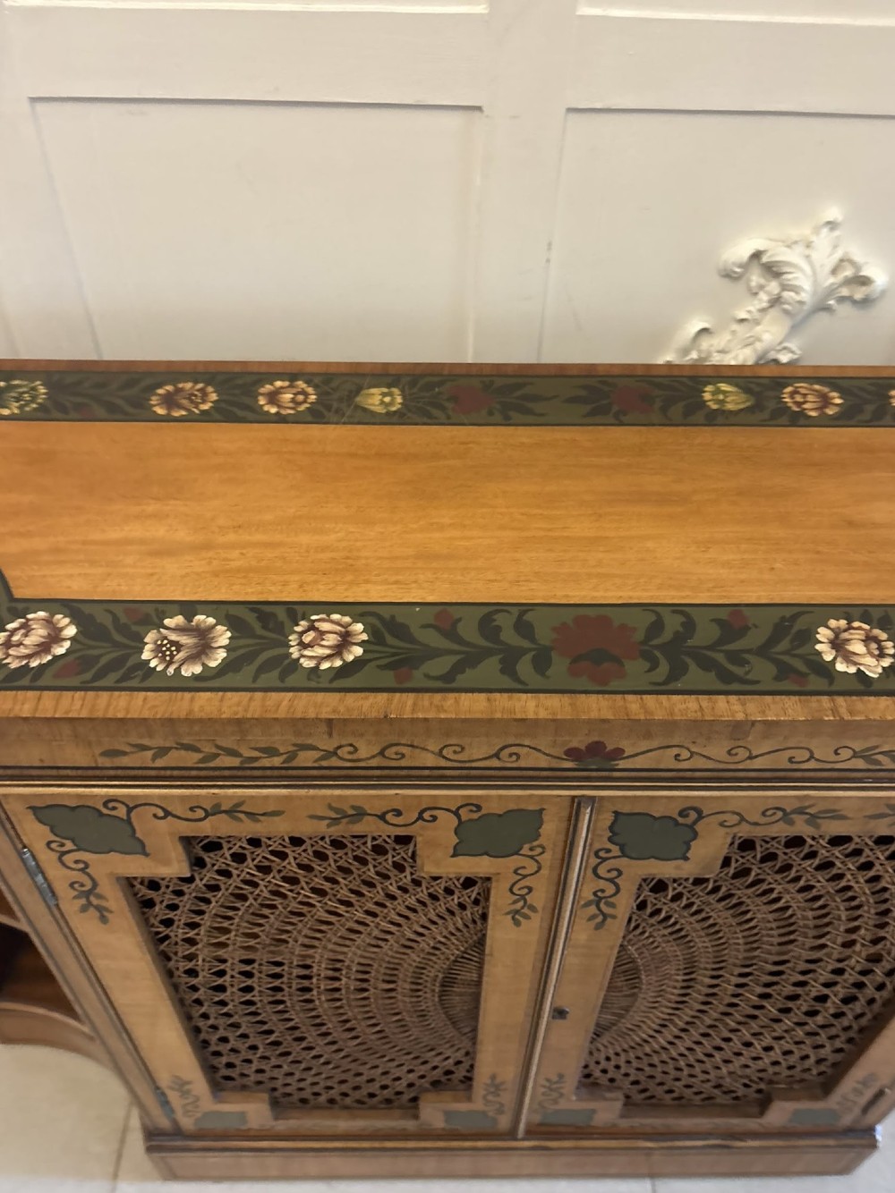 A Sheraton Revival satinwood side cabinet featuring painted leaf borders, central doors with fan-shaped woven cane panels, and open curved side shelves. View VII