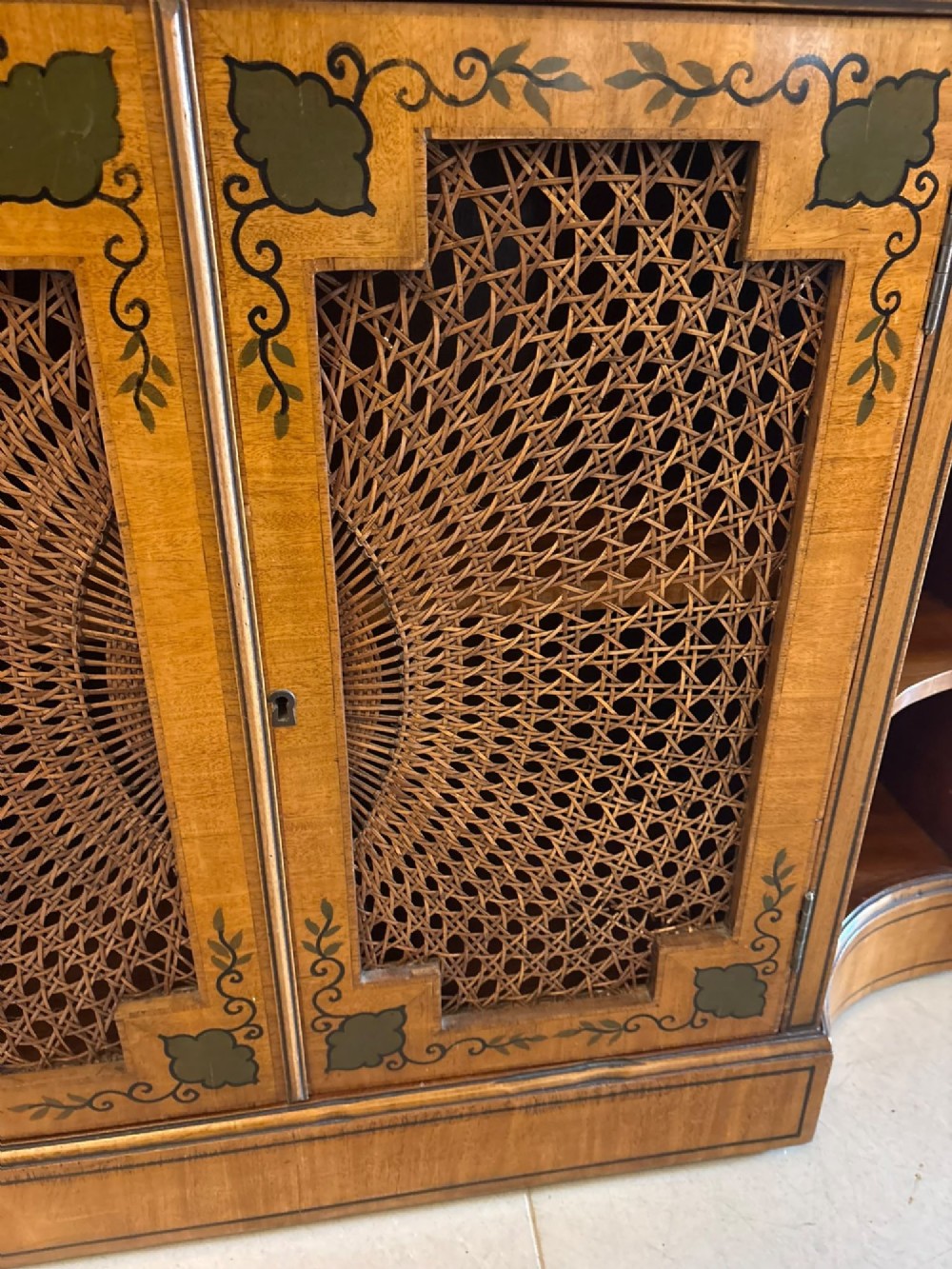 A Sheraton Revival satinwood side cabinet featuring painted leaf borders, central doors with fan-shaped woven cane panels, and open curved side shelves. View XIII