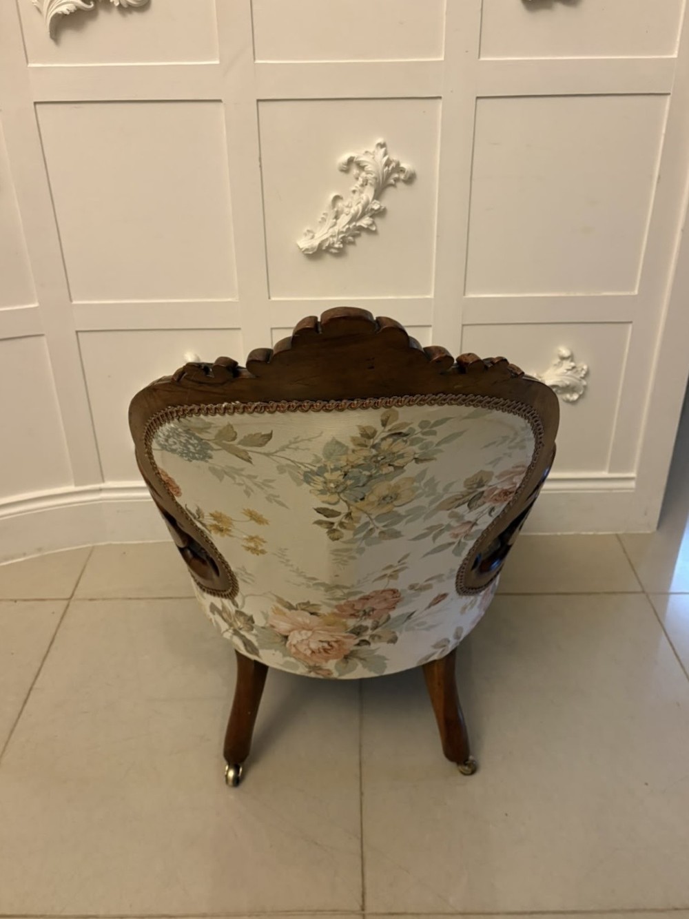 A Victorian walnut armchair featuring floral button-tufted upholstery, carved open scroll arms, and front legs set on brass castors. View V