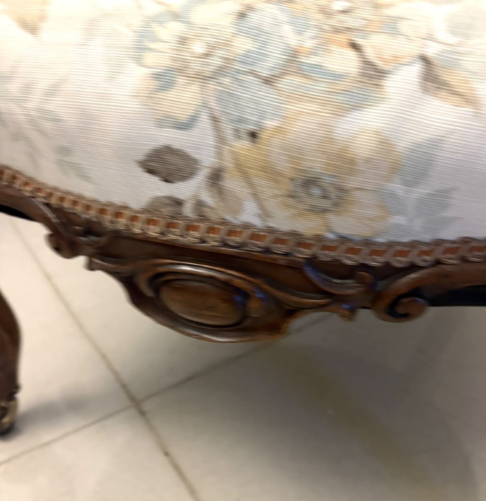 A Victorian walnut armchair featuring floral button-tufted upholstery, carved open scroll arms, and front legs set on brass castors. View VII