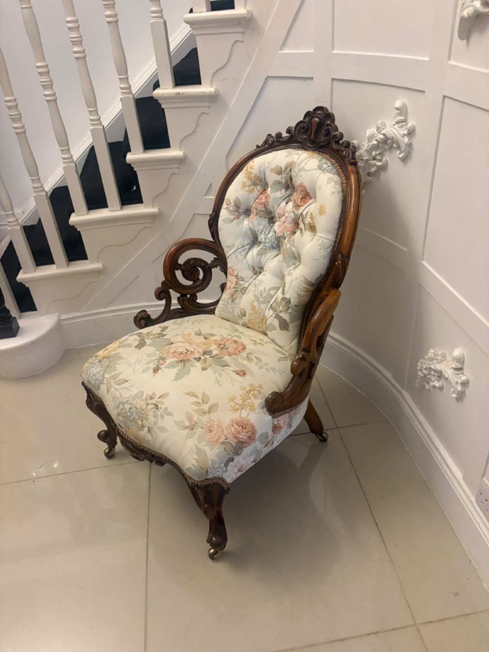 A Victorian walnut armchair featuring floral button-tufted upholstery, carved open scroll arms, and front legs set on brass castors. View XI