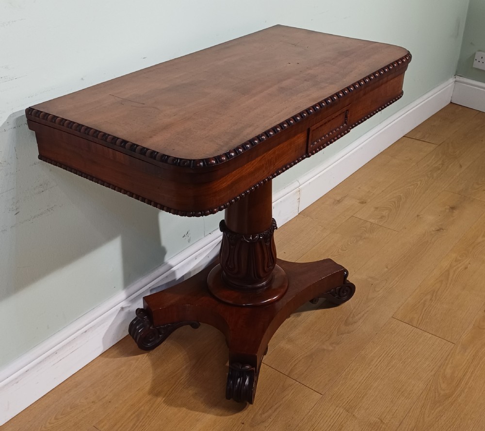 A nineteenth-century mahogany fold-over card table featuring a rectangular top with rounded corners, bead moulding along the frieze, a turned pedestal column, and a quadripartite base with carved scroll feet. View II