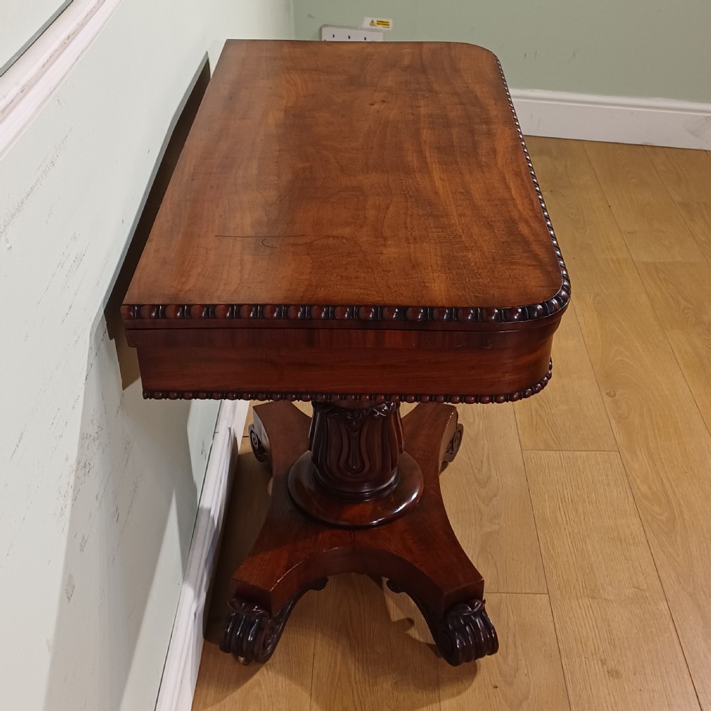A nineteenth-century mahogany fold-over card table featuring a rectangular top with rounded corners, bead moulding along the frieze, a turned pedestal column, and a quadripartite base with carved scroll feet. View V