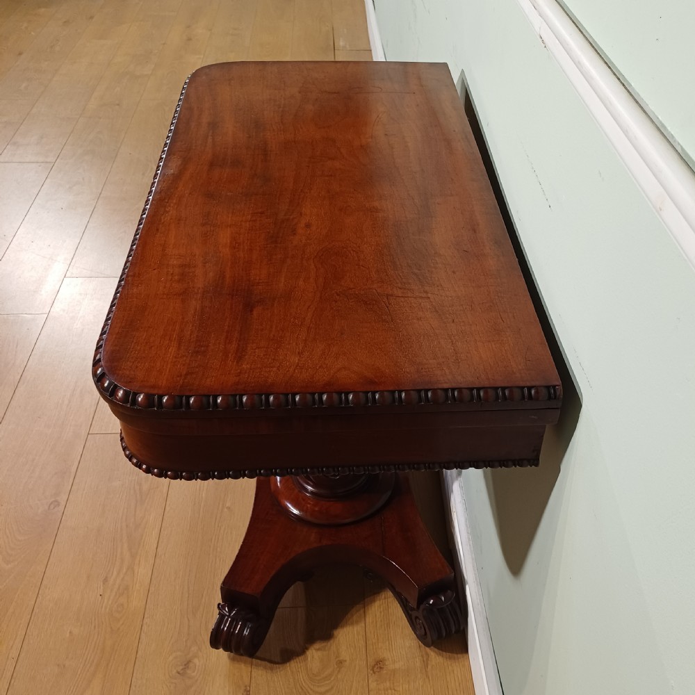 A nineteenth-century mahogany fold-over card table featuring a rectangular top with rounded corners, bead moulding along the frieze, a turned pedestal column, and a quadripartite base with carved scroll feet. View VI