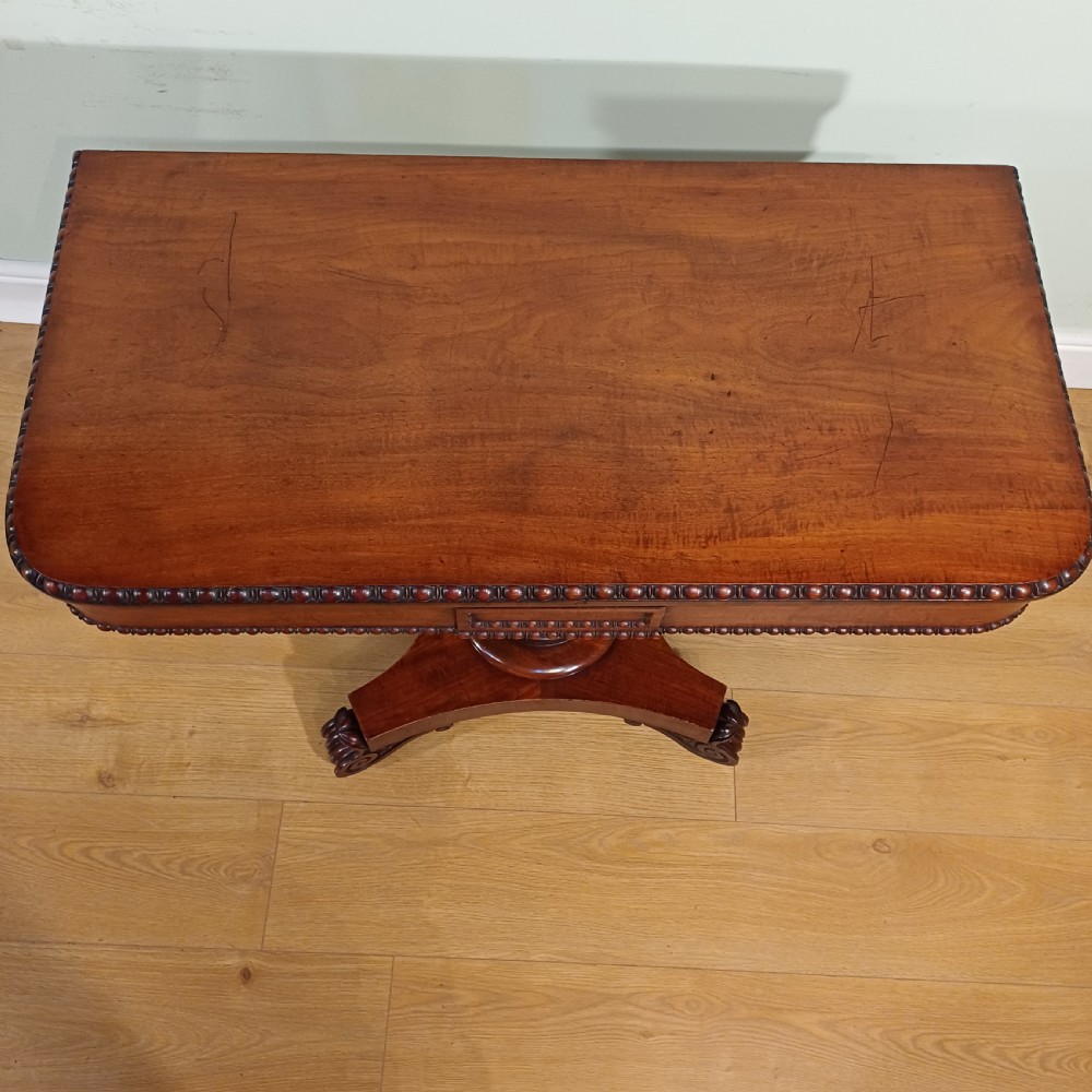 A nineteenth-century mahogany fold-over card table featuring a rectangular top with rounded corners, bead moulding along the frieze, a turned pedestal column, and a quadripartite base with carved scroll feet. View VII