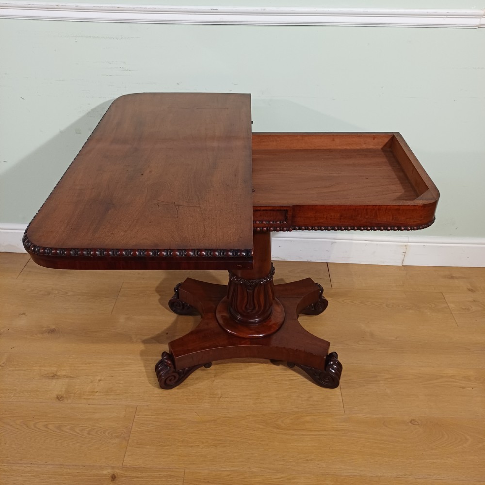 A nineteenth-century mahogany fold-over card table featuring a rectangular top with rounded corners, bead moulding along the frieze, a turned pedestal column, and a quadripartite base with carved scroll feet. View VIII