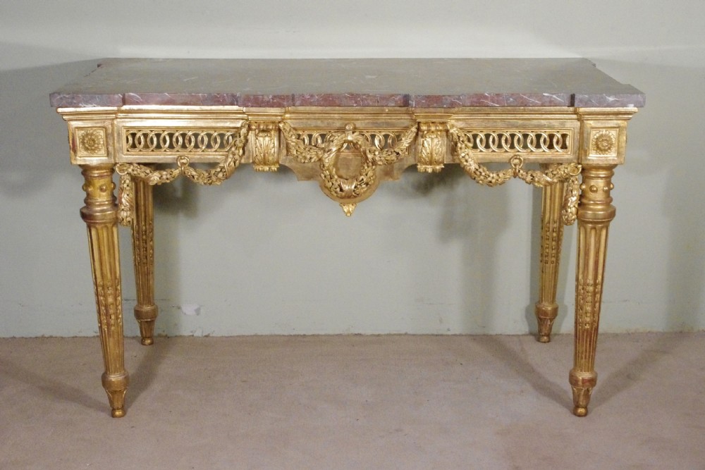 A Louis XVI style giltwood console table with a red veined marble top, carved floral drapes, an openwork frieze, and turned tapered legs.