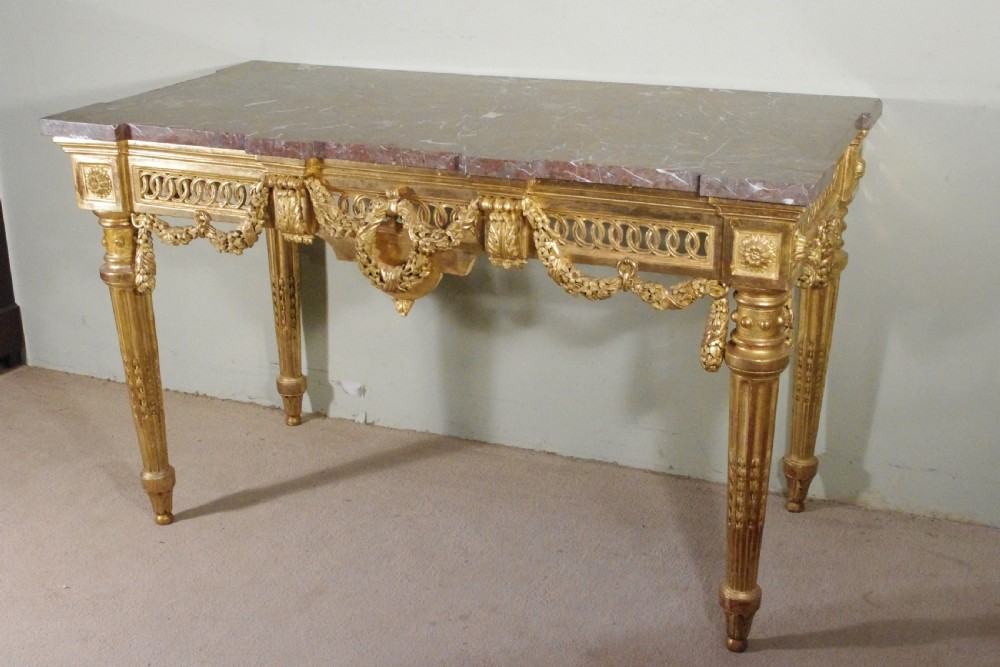A Louis XVI style giltwood console table with a red veined marble top, carved floral drapes, an openwork frieze, and turned tapered legs. View V