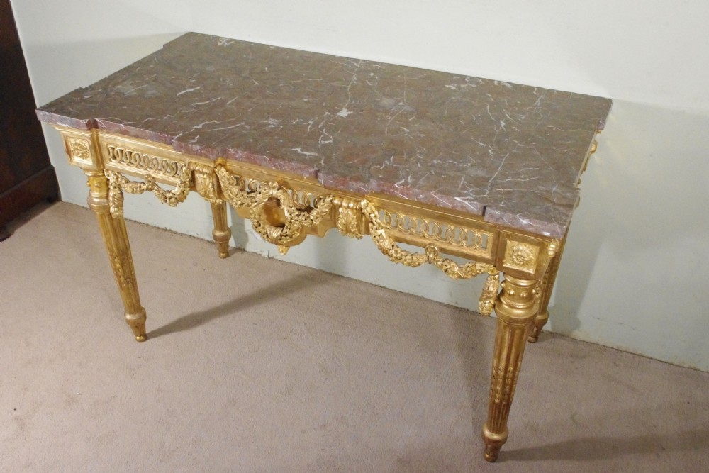 A Louis XVI style giltwood console table with a red veined marble top, carved floral drapes, an openwork frieze, and turned tapered legs. View VI
