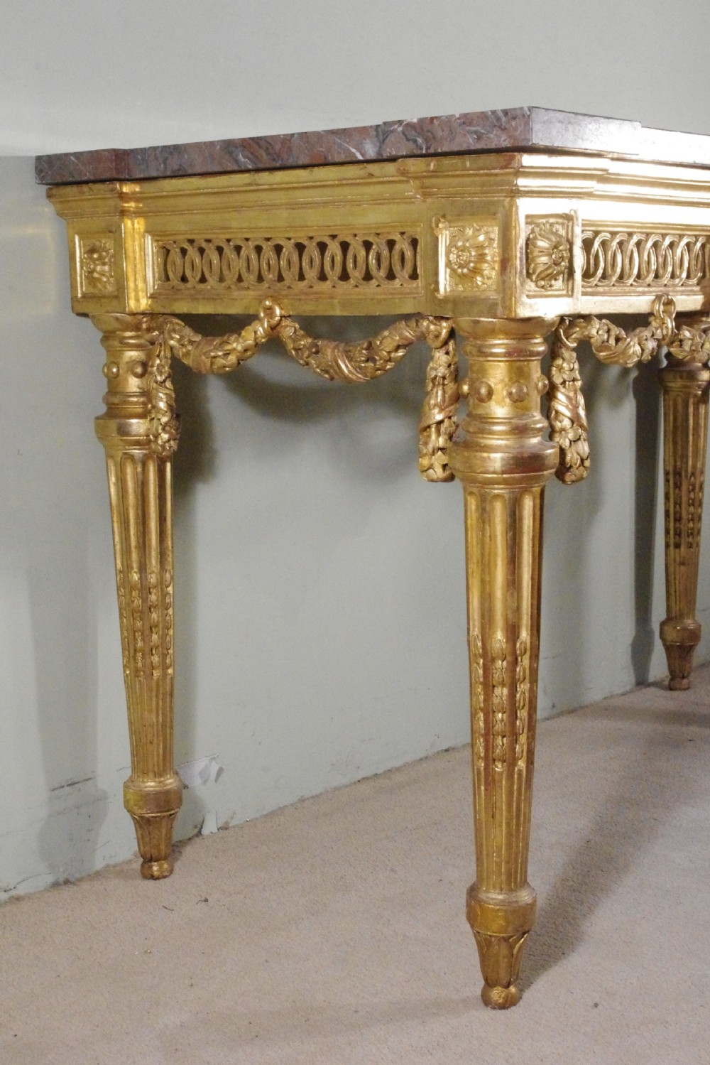 A Louis XVI style giltwood console table with a red veined marble top, carved floral drapes, an openwork frieze, and turned tapered legs. View VII