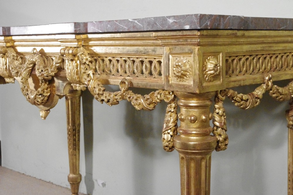 A Louis XVI style giltwood console table with a red veined marble top, carved floral drapes, an openwork frieze, and turned tapered legs. View IX