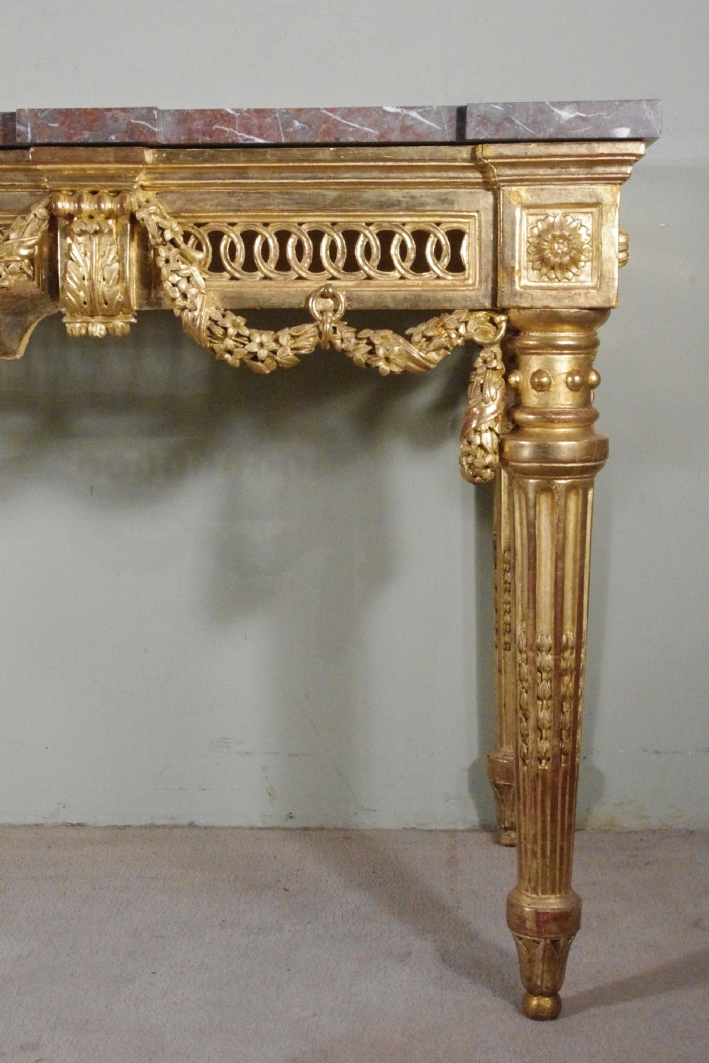 A Louis XVI style giltwood console table with a red veined marble top, carved floral drapes, an openwork frieze, and turned tapered legs. View XI