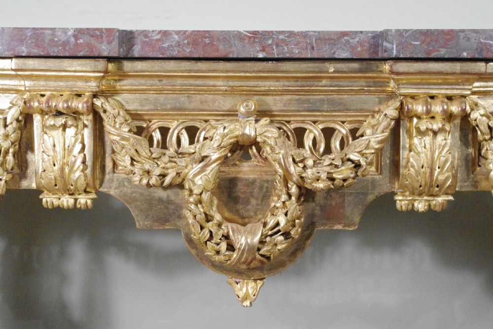 A Louis XVI style giltwood console table with a red veined marble top, carved floral drapes, an openwork frieze, and turned tapered legs. View XIV