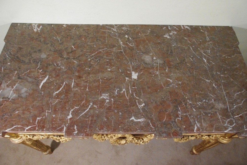 A Louis XVI style giltwood console table with a red veined marble top, carved floral drapes, an openwork frieze, and turned tapered legs. View XVII