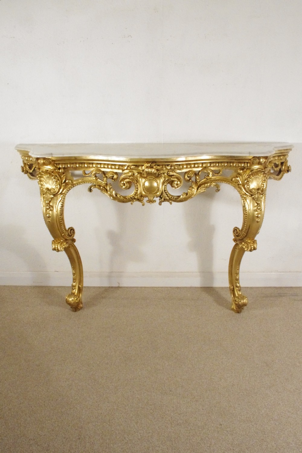 A 19th-century Rococo Revival giltwood console table featuring an ornate carved apron, cabriole legs, and a shaped white marble top.