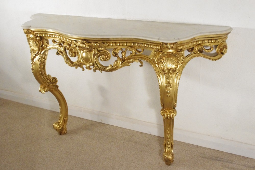 A 19th-century Rococo Revival giltwood console table featuring an ornate carved apron, cabriole legs, and a shaped white marble top. View V