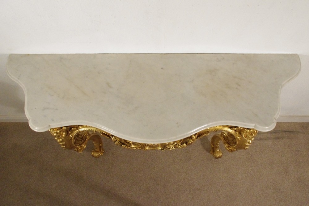 A 19th-century Rococo Revival giltwood console table featuring an ornate carved apron, cabriole legs, and a shaped white marble top. View XIX