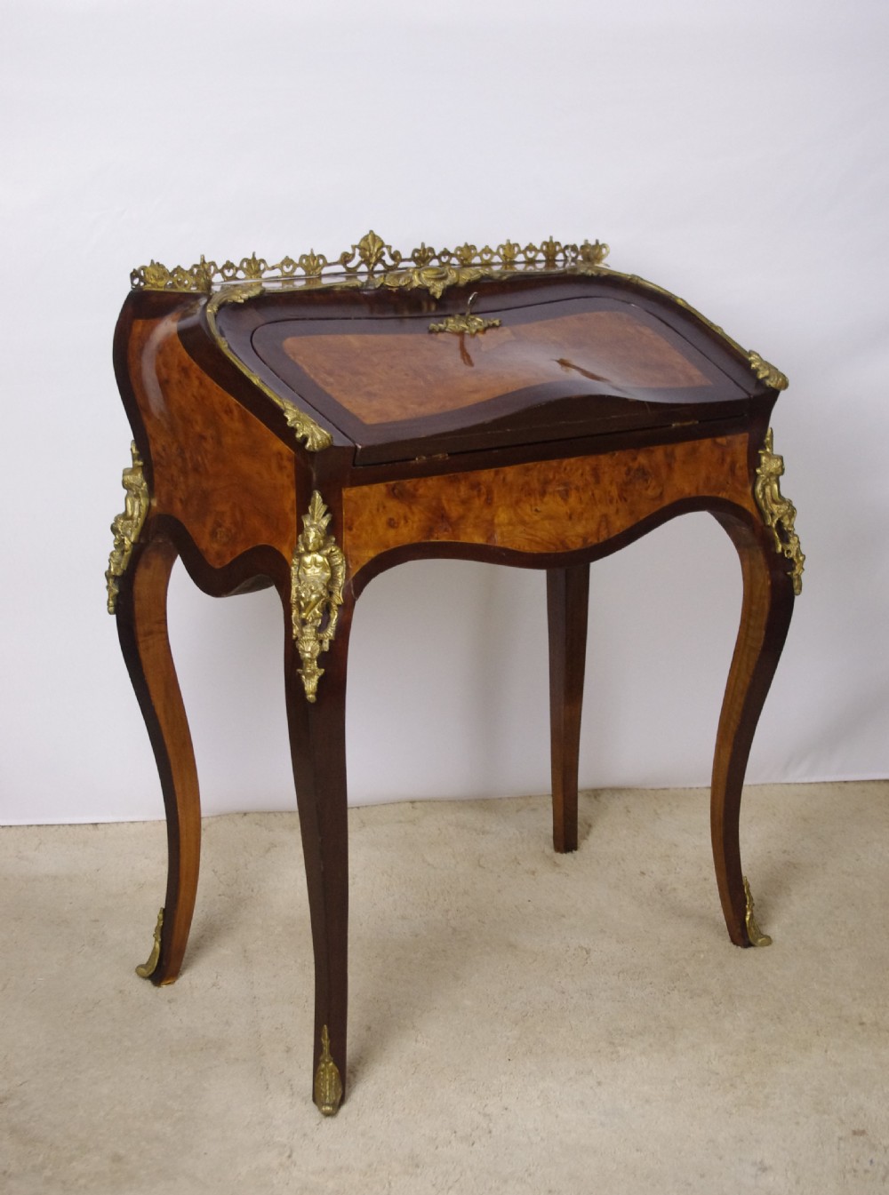 A French Louis XV style bureau de dame constructed from burr walnut veneer with cabriole legs and ornate gilt metal mounts.