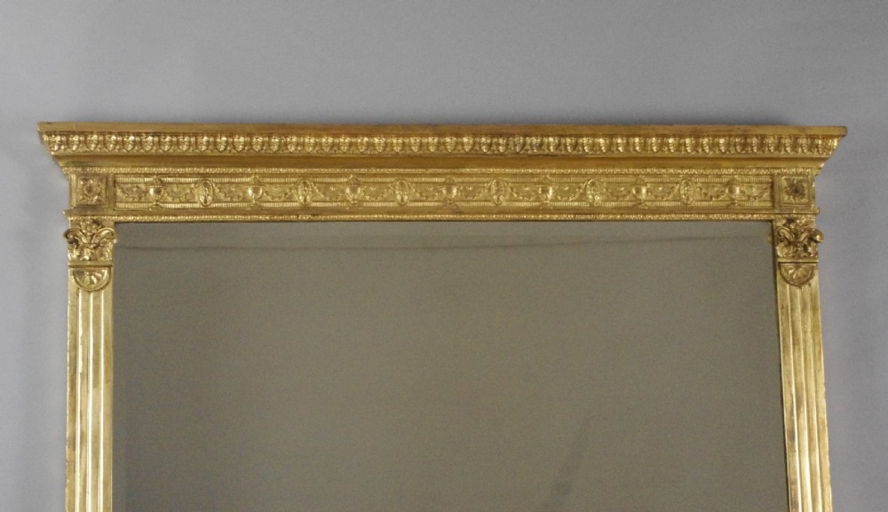 A large rectangular giltwood overmantel mirror in the Neoclassical style featuring fluted pilasters, classical frieze moulding, and decorative base scrolls. View II