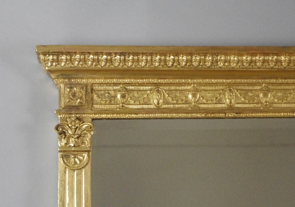 A large rectangular giltwood overmantel mirror in the Neoclassical style featuring fluted pilasters, classical frieze moulding, and decorative base scrolls. View IV