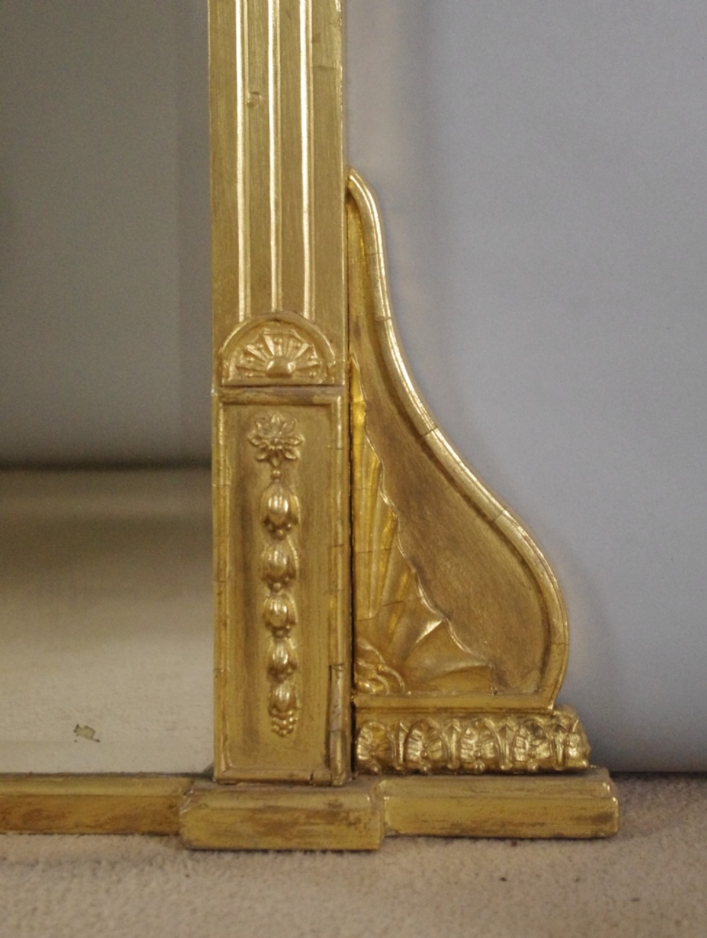 A large rectangular giltwood overmantel mirror in the Neoclassical style featuring fluted pilasters, classical frieze moulding, and decorative base scrolls. View VI