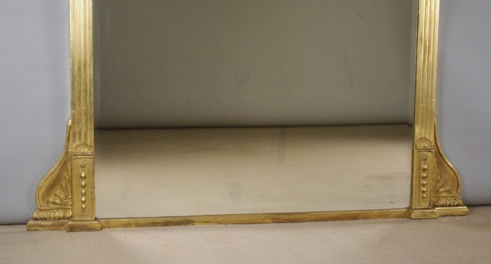 A large rectangular giltwood overmantel mirror in the Neoclassical style featuring fluted pilasters, classical frieze moulding, and decorative base scrolls. View VII
