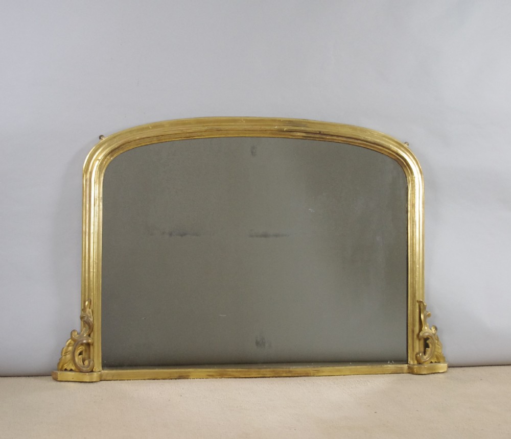 A Victorian giltwood overmantel mirror featuring a gently arched top frame and carved acanthus scroll corner details.