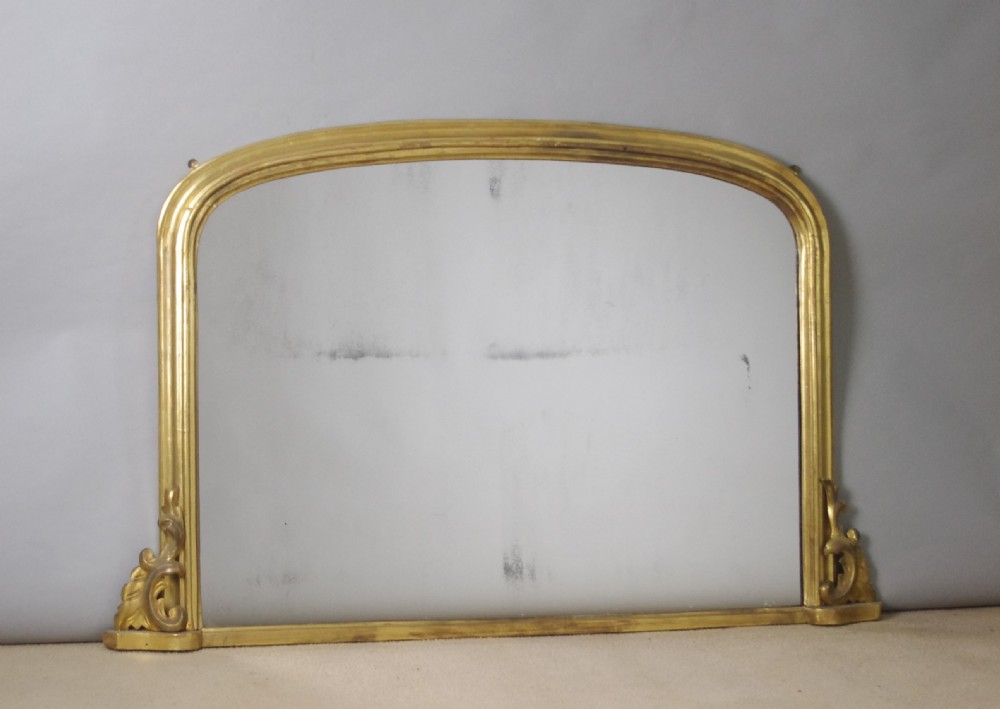 A Victorian giltwood overmantel mirror featuring a gently arched top frame and carved acanthus scroll corner details. View VI