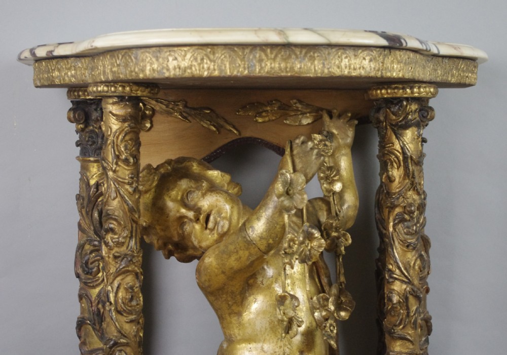 A 19th-century giltwood console table featuring a central carved putto figure with floral accents beneath a shaped marble top. View VII