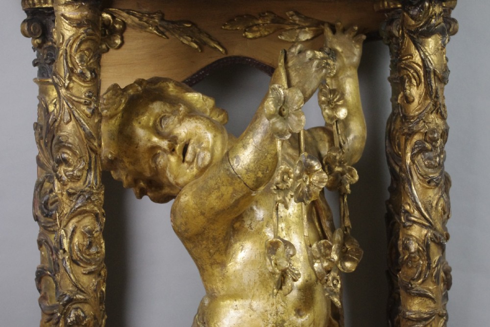 A 19th-century giltwood console table featuring a central carved putto figure with floral accents beneath a shaped marble top. View VIII