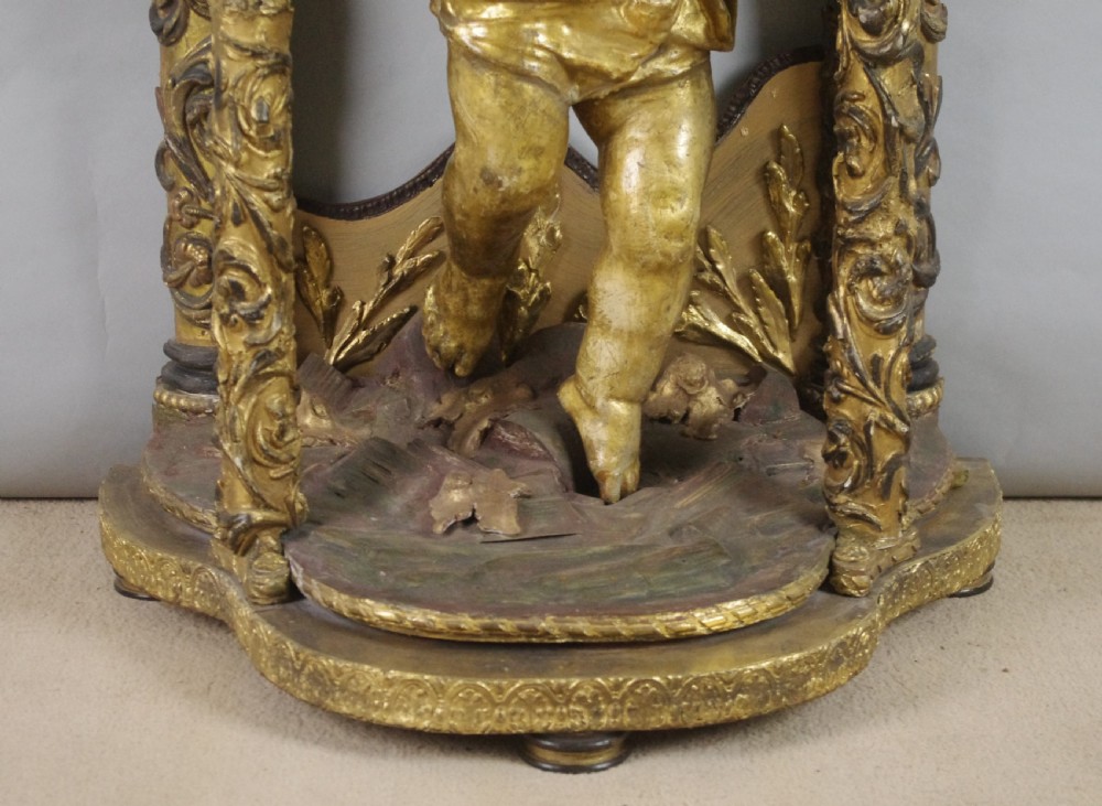 A 19th-century giltwood console table featuring a central carved putto figure with floral accents beneath a shaped marble top. View IX