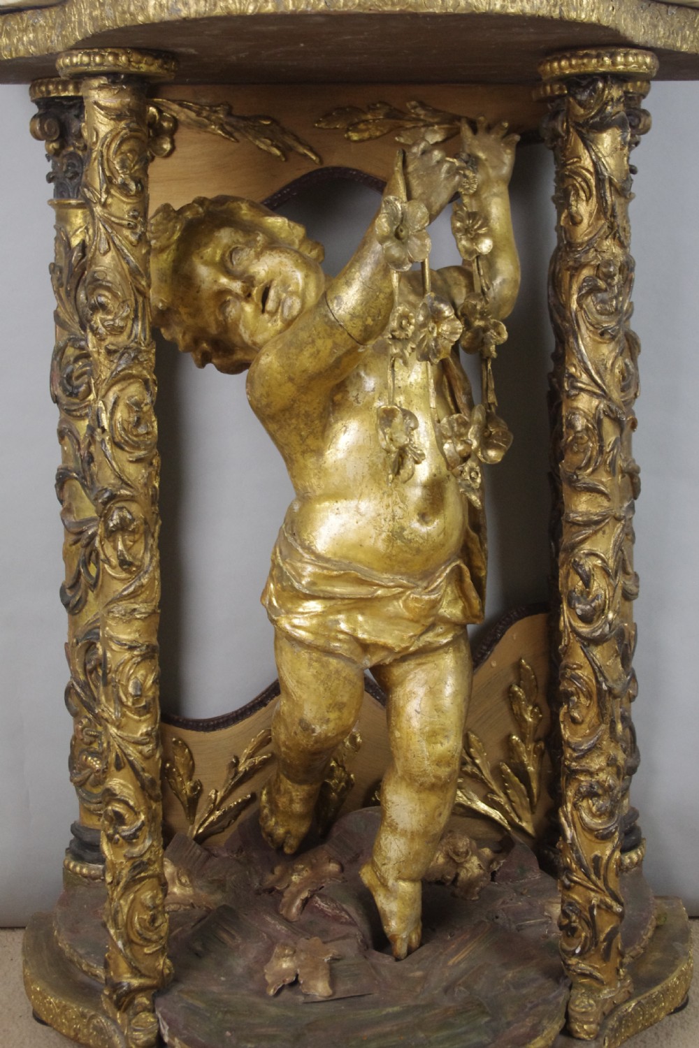A 19th-century giltwood console table featuring a central carved putto figure with floral accents beneath a shaped marble top. View XI