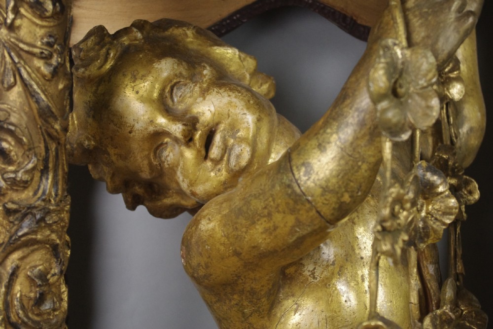 A 19th-century giltwood console table featuring a central carved putto figure with floral accents beneath a shaped marble top. View XIV