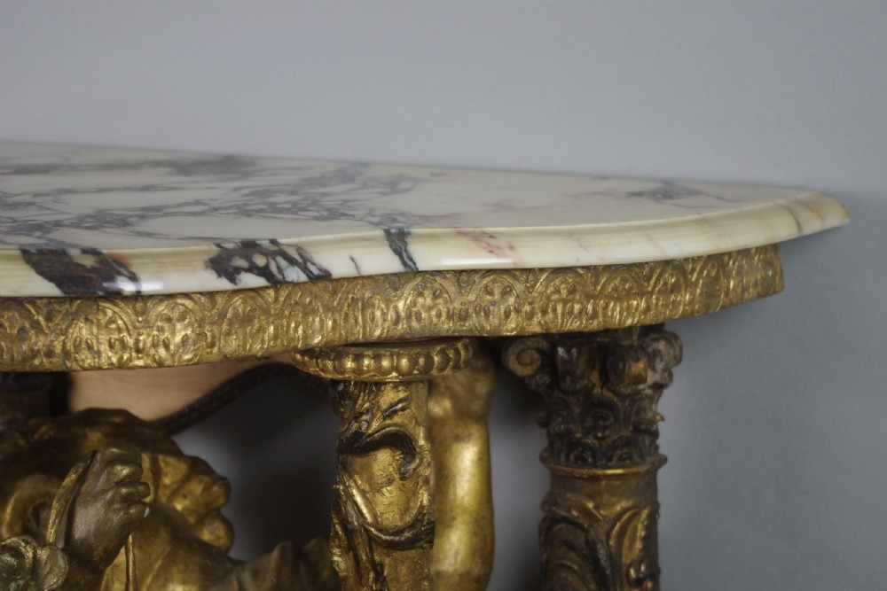 A 19th-century giltwood console table featuring a central carved putto figure with floral accents beneath a shaped marble top. View XV