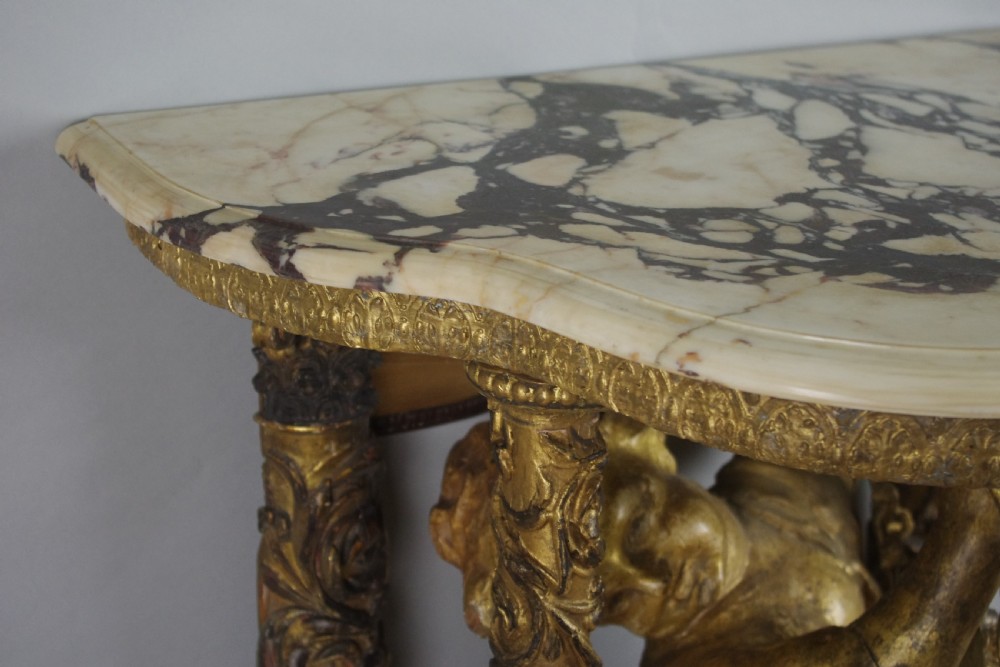 A 19th-century giltwood console table featuring a central carved putto figure with floral accents beneath a shaped marble top. View XVI