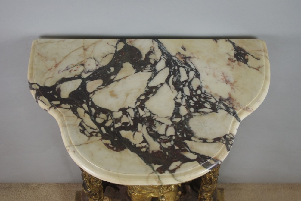 A 19th-century giltwood console table featuring a central carved putto figure with floral accents beneath a shaped marble top. View XVII