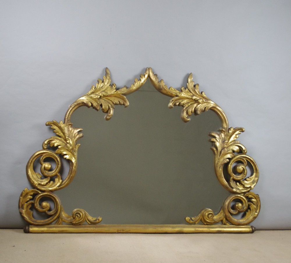 An ornate French giltwood overmantel mirror featuring carved acanthus leaf cresting along an arched frame with a straight base rail.