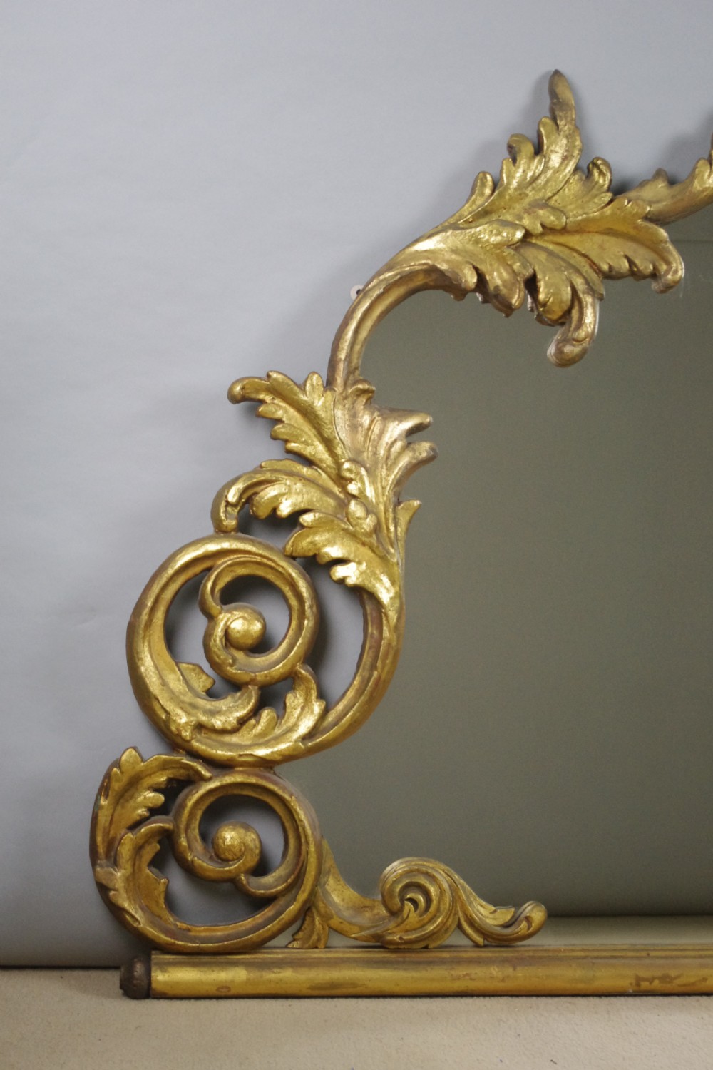 An ornate French giltwood overmantel mirror featuring carved acanthus leaf cresting along an arched frame with a straight base rail. View II