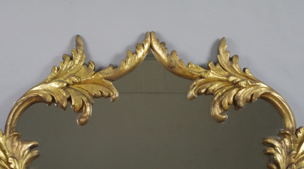 An ornate French giltwood overmantel mirror featuring carved acanthus leaf cresting along an arched frame with a straight base rail. View IV