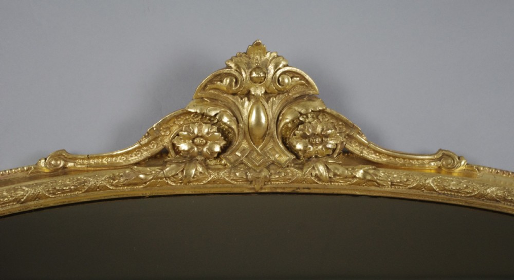 A large Victorian arched gilt overmantle mirror featuring an ornate central floral crest and beaded detail along the frame. View III
