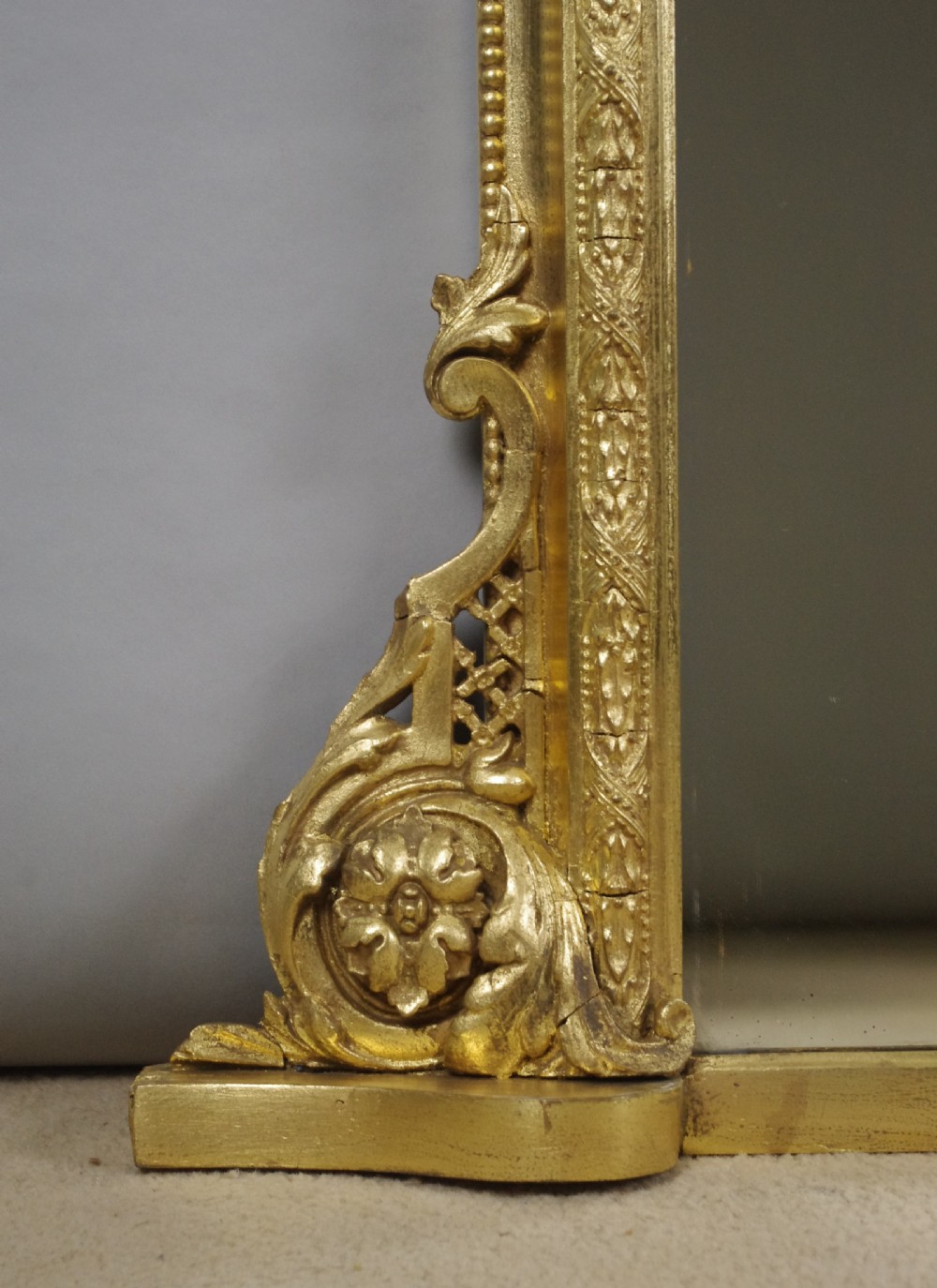 A large Victorian arched gilt overmantle mirror featuring an ornate central floral crest and beaded detail along the frame. View VII