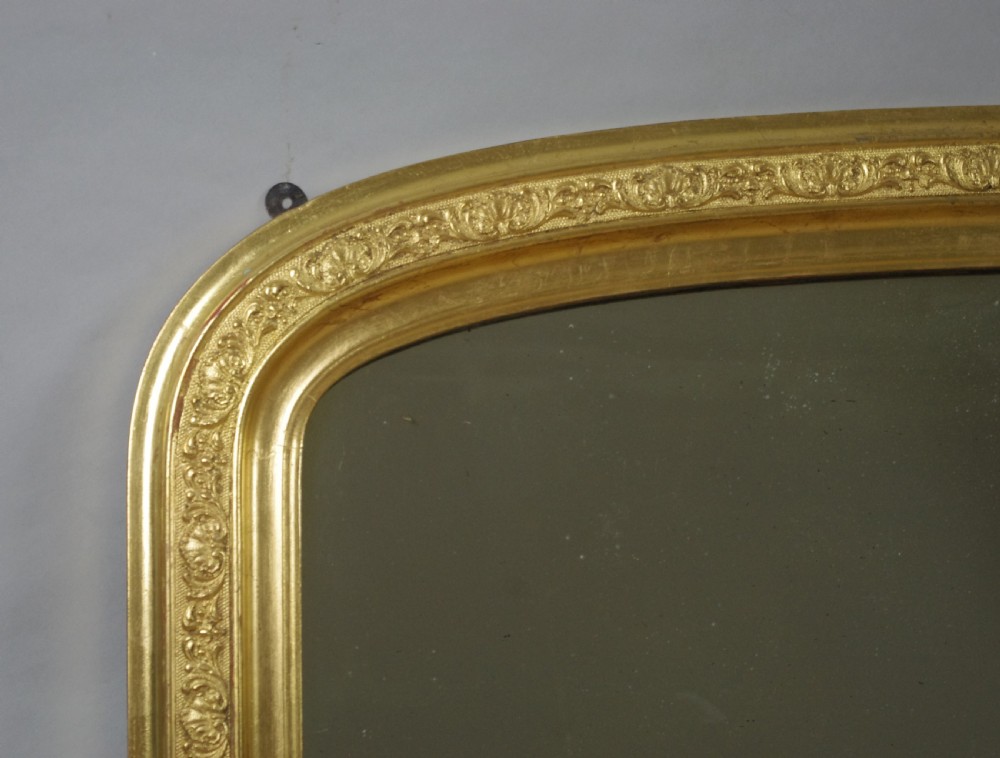 A large Victorian gold gilded overmantel mirror featuring an arched upper frame decorated with relief moulded floral scrollwork. View IV