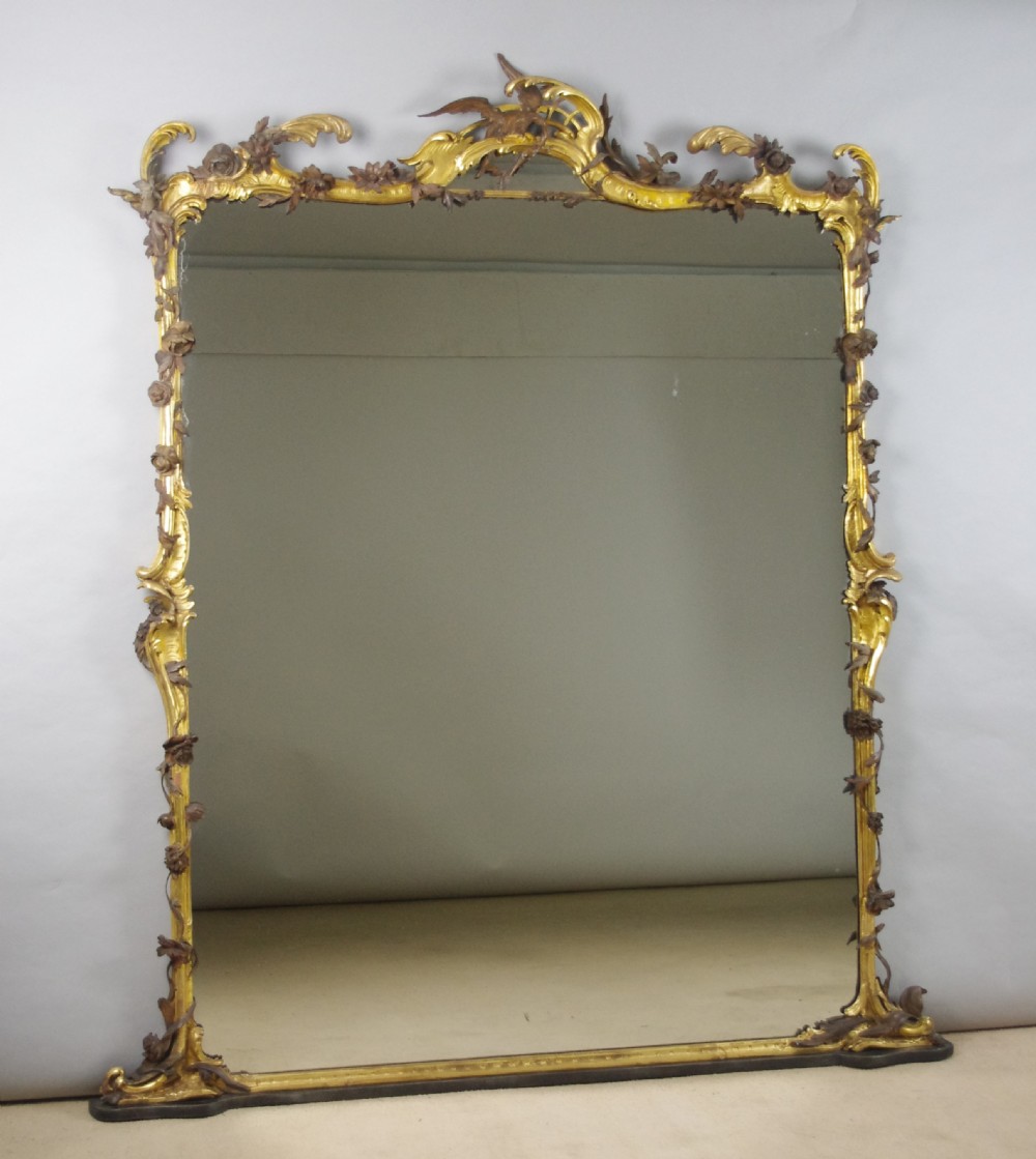Large Victorian Rococo style giltwood overmantel mirror featuring elaborate carved foliate trails, asymmetric C-scrolls, and a scrolling top crest.