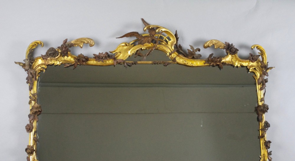 Large Victorian Rococo style giltwood overmantel mirror featuring elaborate carved foliate trails, asymmetric C-scrolls, and a scrolling top crest. View II