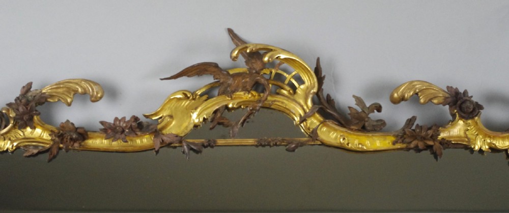 Large Victorian Rococo style giltwood overmantel mirror featuring elaborate carved foliate trails, asymmetric C-scrolls, and a scrolling top crest. View III