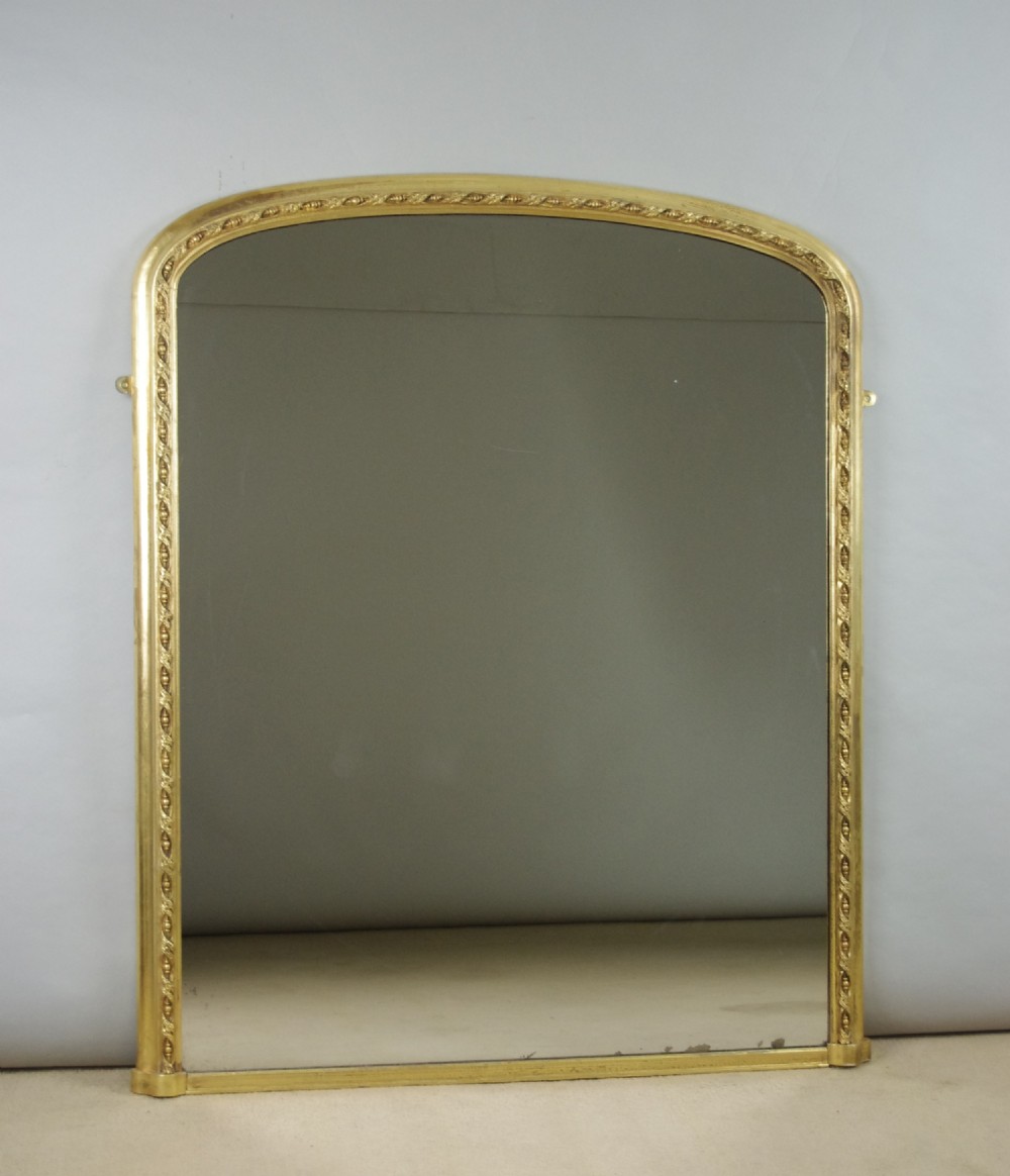 A large Victorian arched overmantel mirror featuring a gilded wooden frame decorated with detailed beadwork around the inner rim.