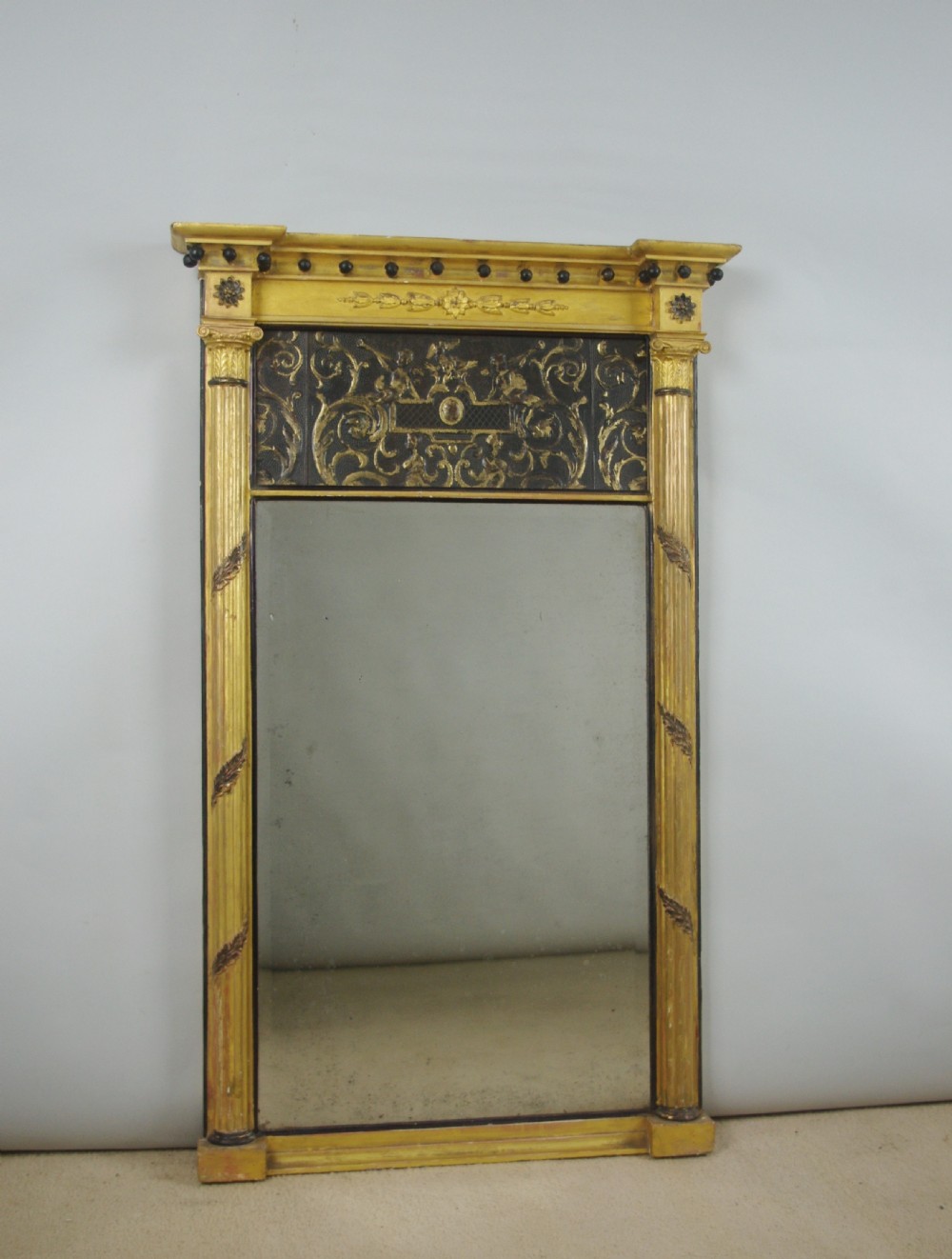 A tall rectangular Regency giltwood pier mirror featuring fluted pilasters, spherule cornice details, and a decorative foliate frieze panel above the glass.