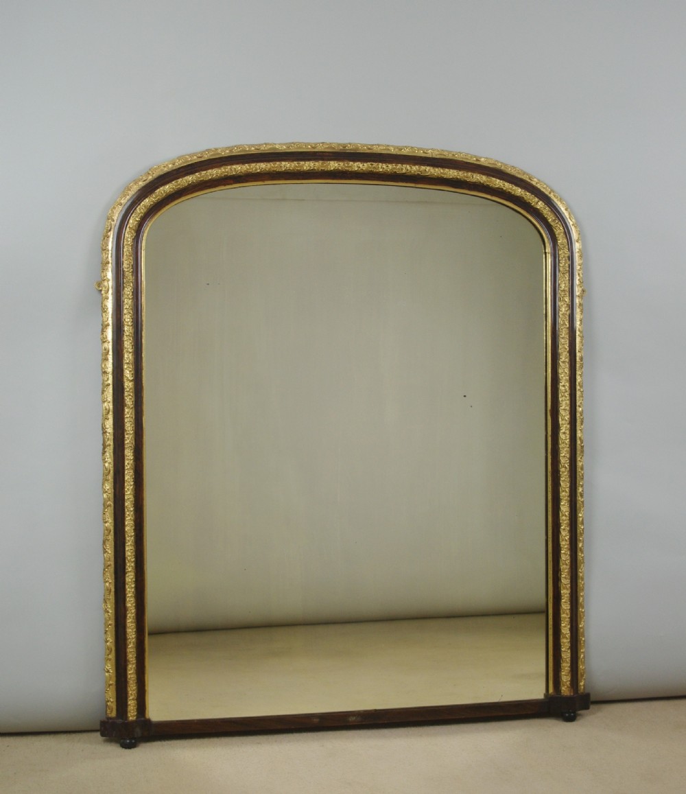 A large Victorian arched overmantel mirror featuring a simulated dark wood frame with detailed parcel-gilt foliage moulding along the inner and outer borders.