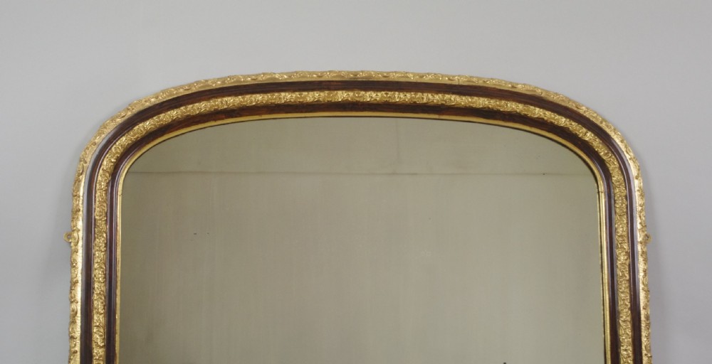 A large Victorian arched overmantel mirror featuring a simulated dark wood frame with detailed parcel-gilt foliage moulding along the inner and outer borders. View II